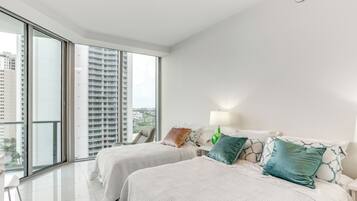 A modern hotel room with two beds, a large window, and a view of tall buildings.