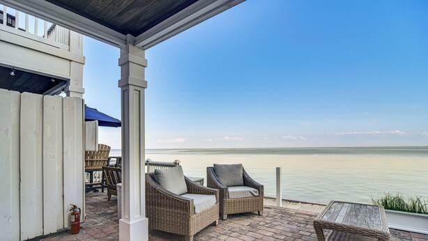 A covered patio with wicker furniture and a view of the water.