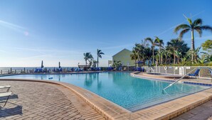 A swimming pool with blue chairs and palm trees, a building in the background, and a clear sky.