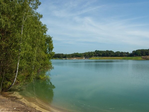 A serene lakeside view with a small building near the water's edge, surrounded by dense trees.
