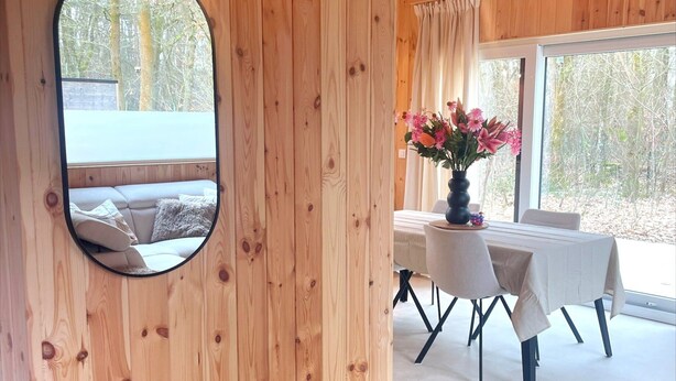 A wooden interior with a round mirror, a dining table with chairs, and a vase of flowers. - Zutendaal Forest Retreat (Zutendaal)