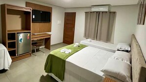 Et hotelværelse med seng, skrivebord, køleskab og klimaanlæg.