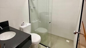 Et badeværelse med en brusekabine i glas, toilet og vask med sort bordplade.