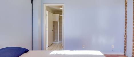 A bedroom with a bed, a blue pillow, a wooden shelf, and a door leading to a bathroom.