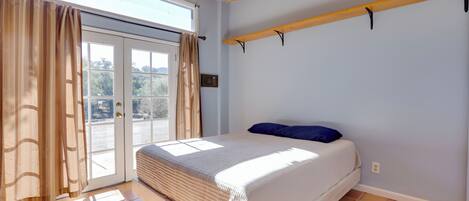 Quarto com uma cama, janela com cortinas, teto de madeira e chão de azulejos.