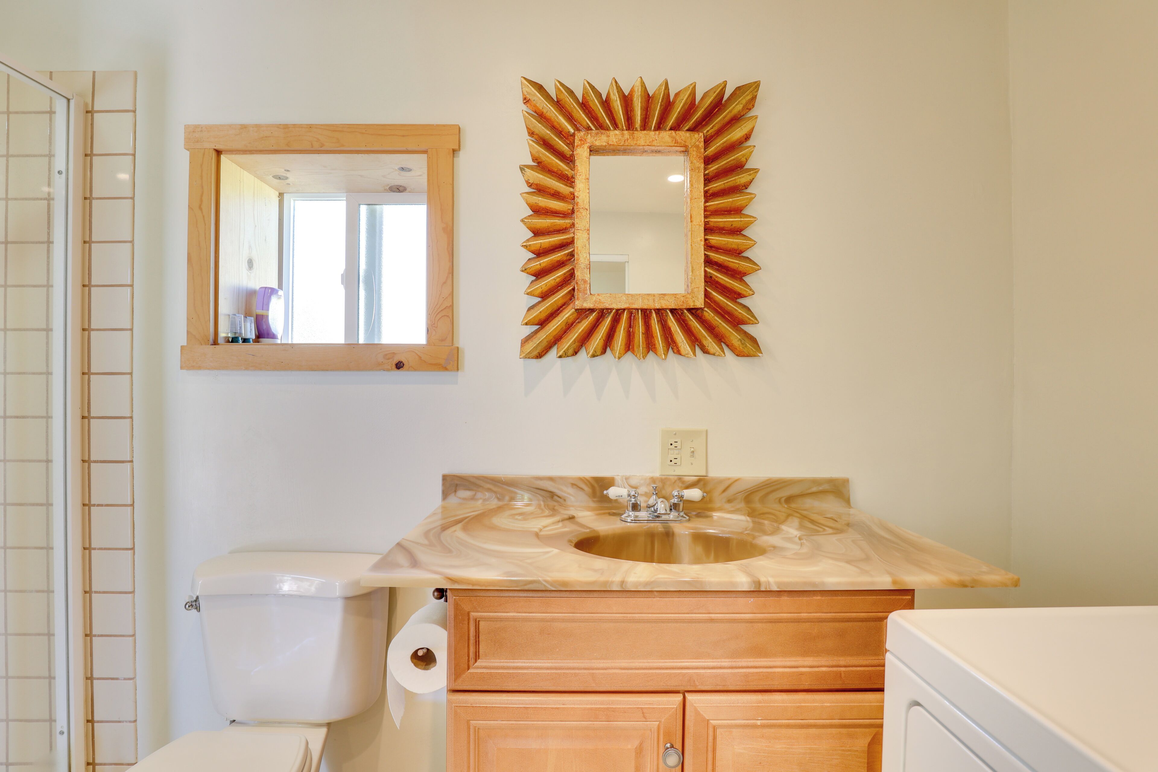 Une salle de bain avec un meuble-lavabo en bois, un évier, des toilettes et un miroir avec un cadre en forme de soleil.