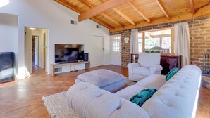 A spacious living room with a wooden ceiling, a large TV, a white sofa, and a stone wall. - 4 Mi to Lake Wohlford: Cabin in Escondido (Valley Center)