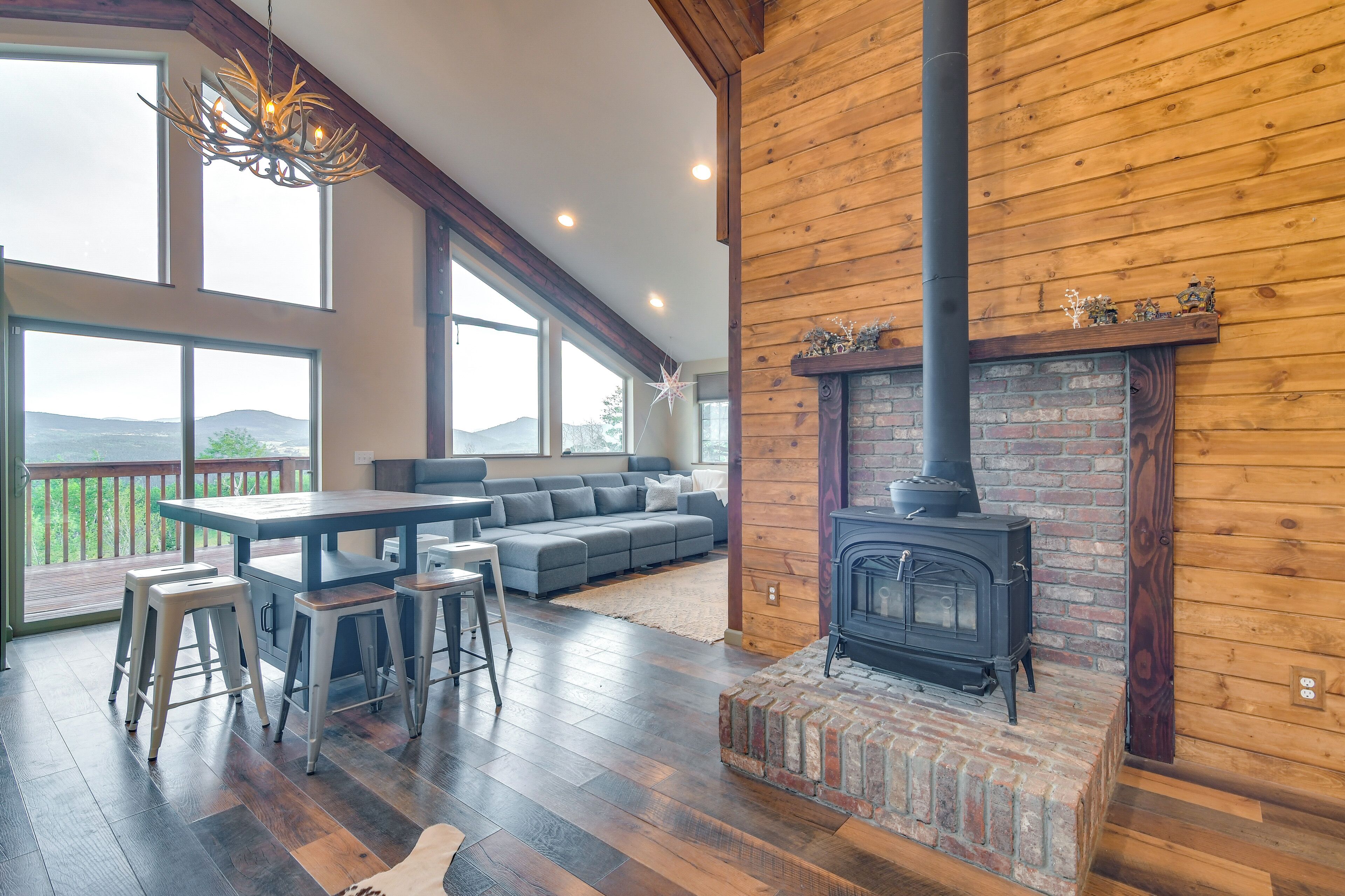 A spacious living area with a fireplace, large windows, and a high ceiling.