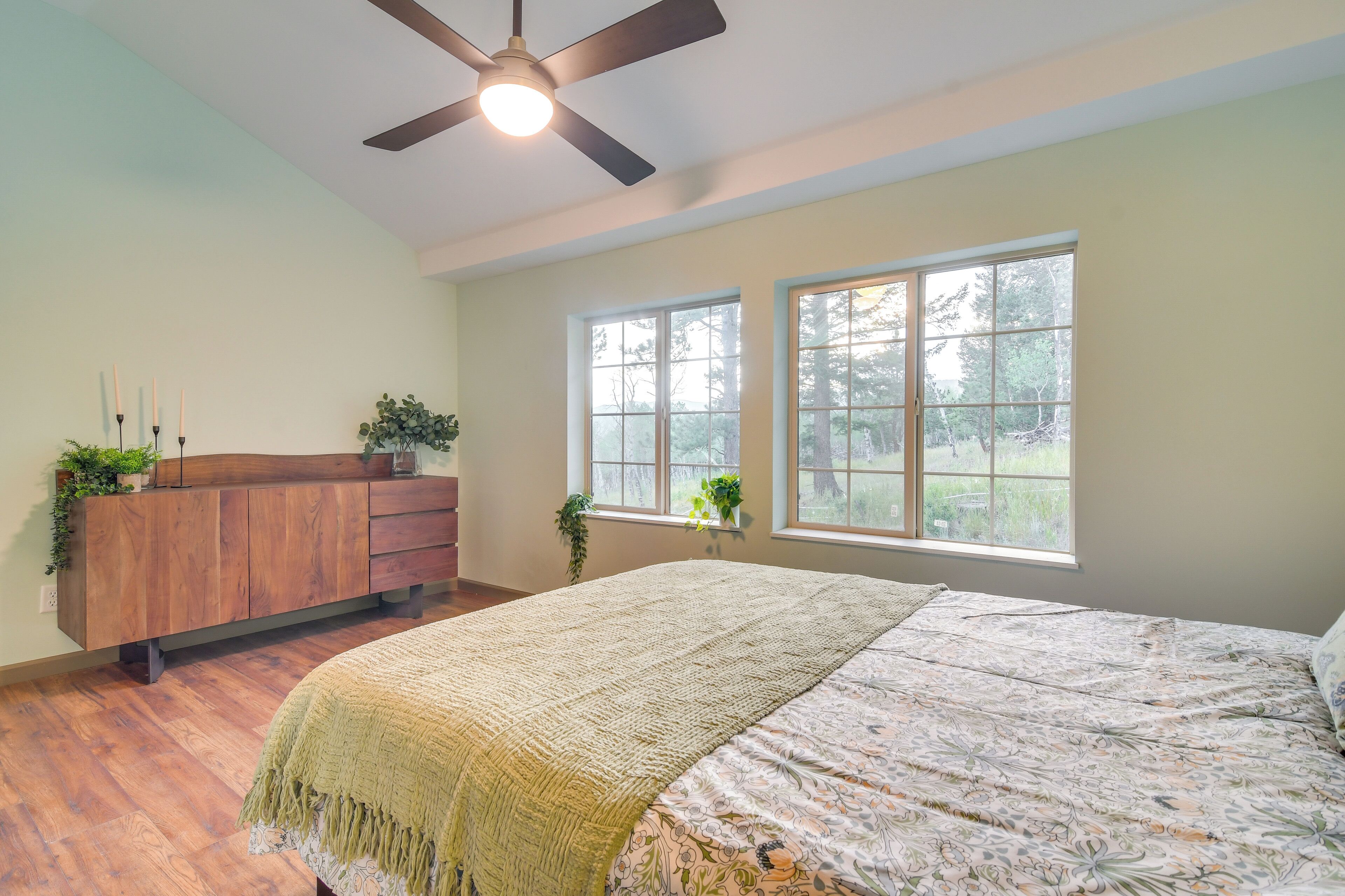 A bedroom with a bed, wooden dresser, two windows, and a ceiling fan.