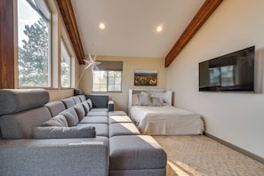 Una sala de estar moderna con un sofá modular, una cama, un televisor y ventanas grandes.