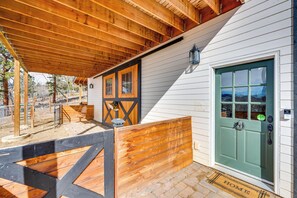 Une terrasse en bois mène à un bâtiment blanc doté d’une porte verte, d’un banc en bois et d’une lanterne.