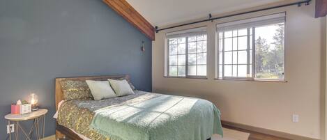 Un dormitorio con cama, mesita de noche, lámpara y ventanas grandes.
