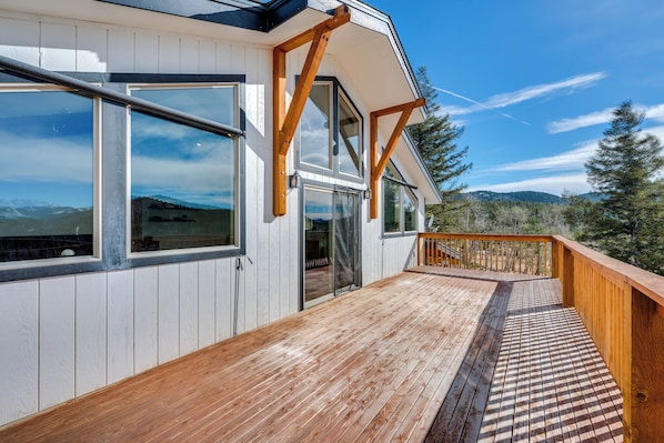 Une terrasse en bois offrant une vue sur les montagnes, un balcon avec des balustrades en bois et de grandes fenêtres.
