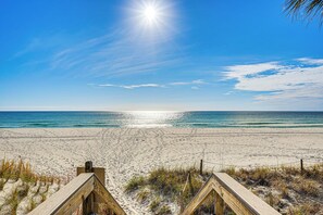A beach with a wooden boardwalk leading to the ocean, clear skies, and a bright sun. - Walk to Beach: PCB Gem w/ Community Pool Access! (Panama City Beach)