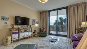 A living room with a flat-screen TV, a sofa, a coffee table, and a balcony with curtains.