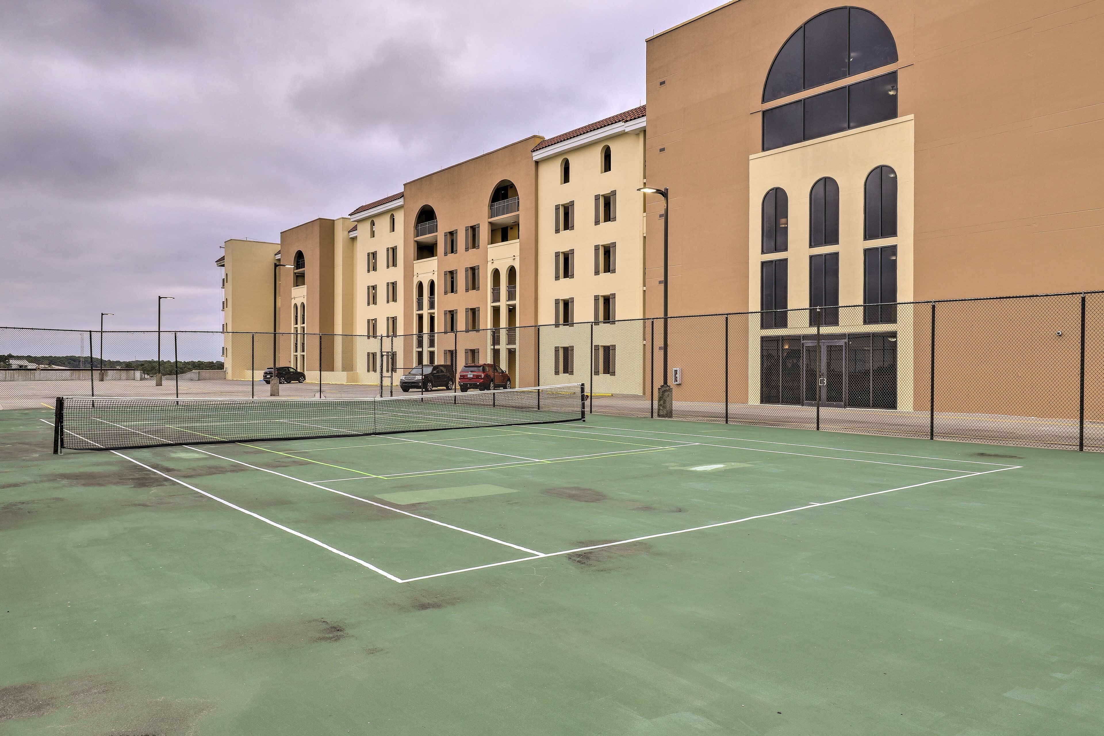 An outdoor tennis court adjacent to a multi-story building with large windows and balconies.