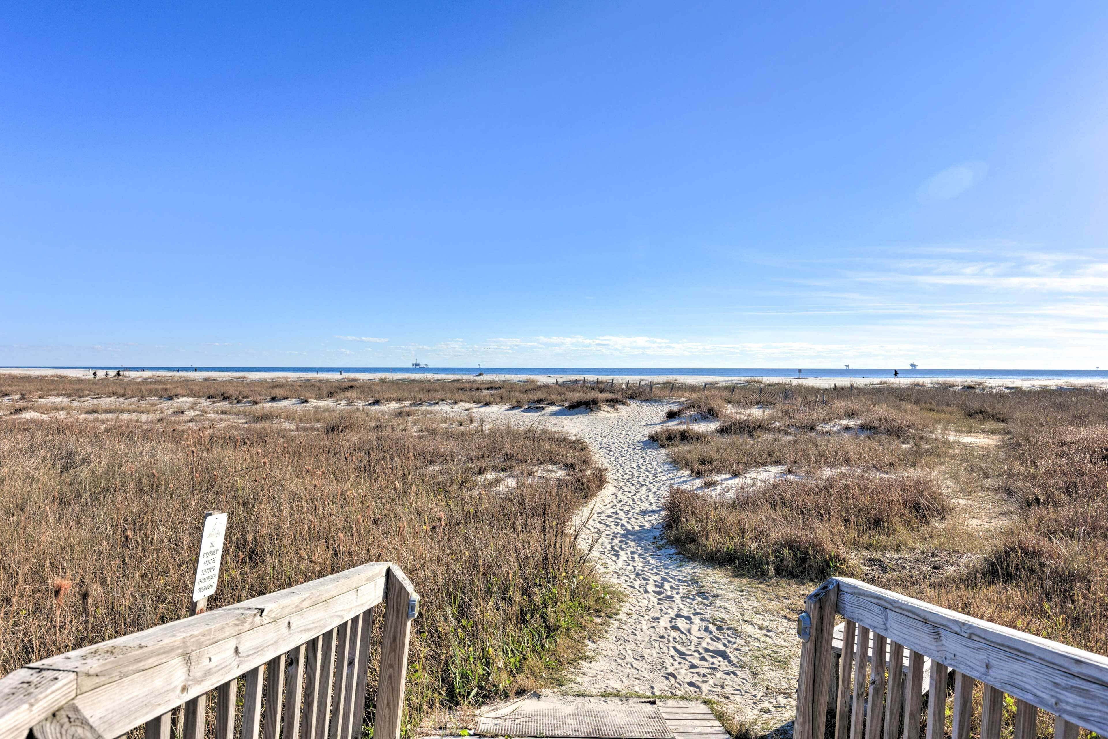 Une promenade en bois menant à une plage où l’on trouve de l’herbe sèche et du sable.
