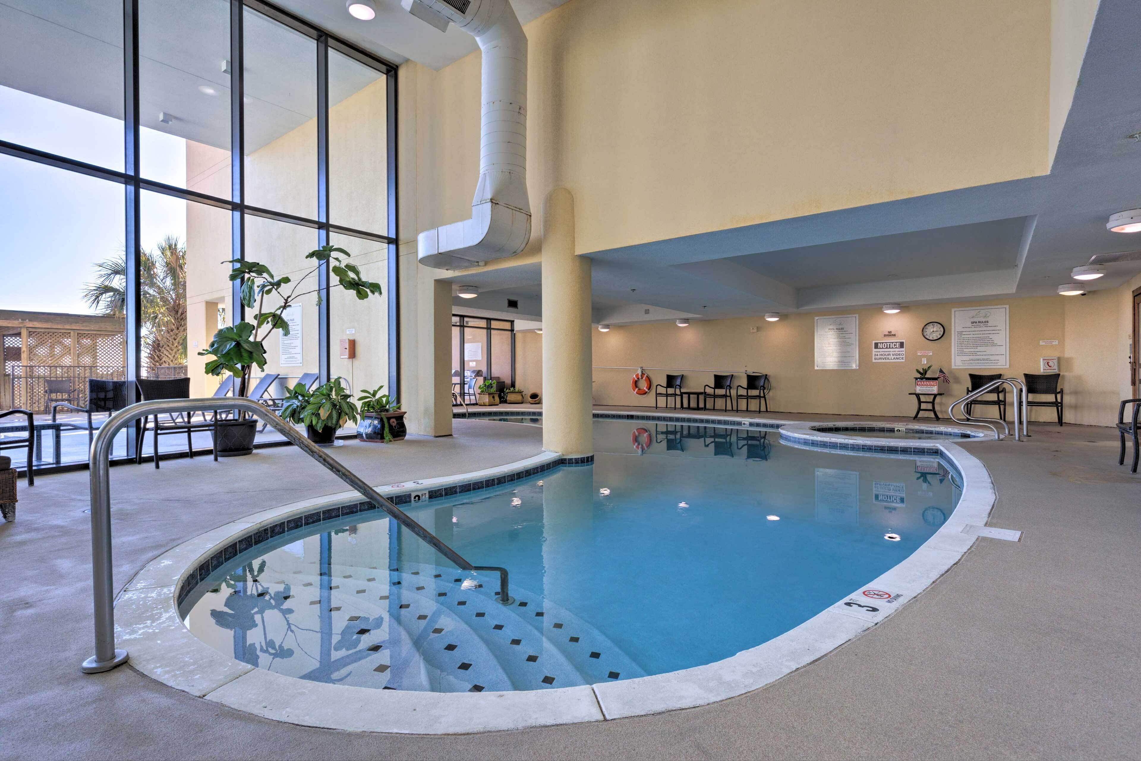 Une piscine intérieure offrant une vue dégagée sur l’extérieur, un espace de détente aménagé au bord de la piscine et une horloge fixée au mur.