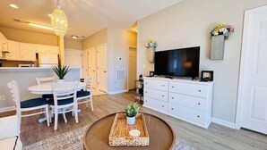 A modern living room with a round coffee table, a flat-screen TV, and a dining area with a white table and chairs. - River Oaks 2BR beautiful condo (Myrtle Beach)