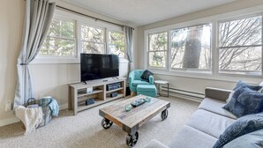 Una sala de estar con un televisor grande, un sofá, una mesa de centro y un ventanal con cortinas.