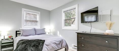 A bedroom with a bed, bedside tables, a dresser, a TV, and windows.