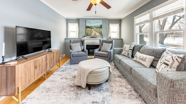 A living room with a flat-screen TV, wooden cabinet, grey sofa, ottoman, and a ceiling fan. - 3 Mi to Hospitals: Inviting Rockford Home w/ Yard! (Rockford)