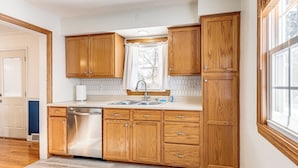 A kitchen with wooden cabinets, a stainless steel dishwasher, and a window with curtains. - 3 Mi to Hospitals: Inviting Rockford Home w/ Yard! (Rockford)