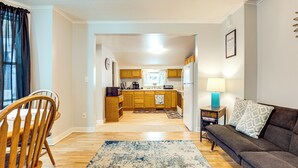 Una cocina moderna con armarios de madera, un comedor con mesa y sillas de madera, y una sala de estar con sofá y alfombra estampada.