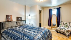 Un dormitorio con una cama grande, una mesita de noche, una lámpara, una silla y una ventana con cortinas.