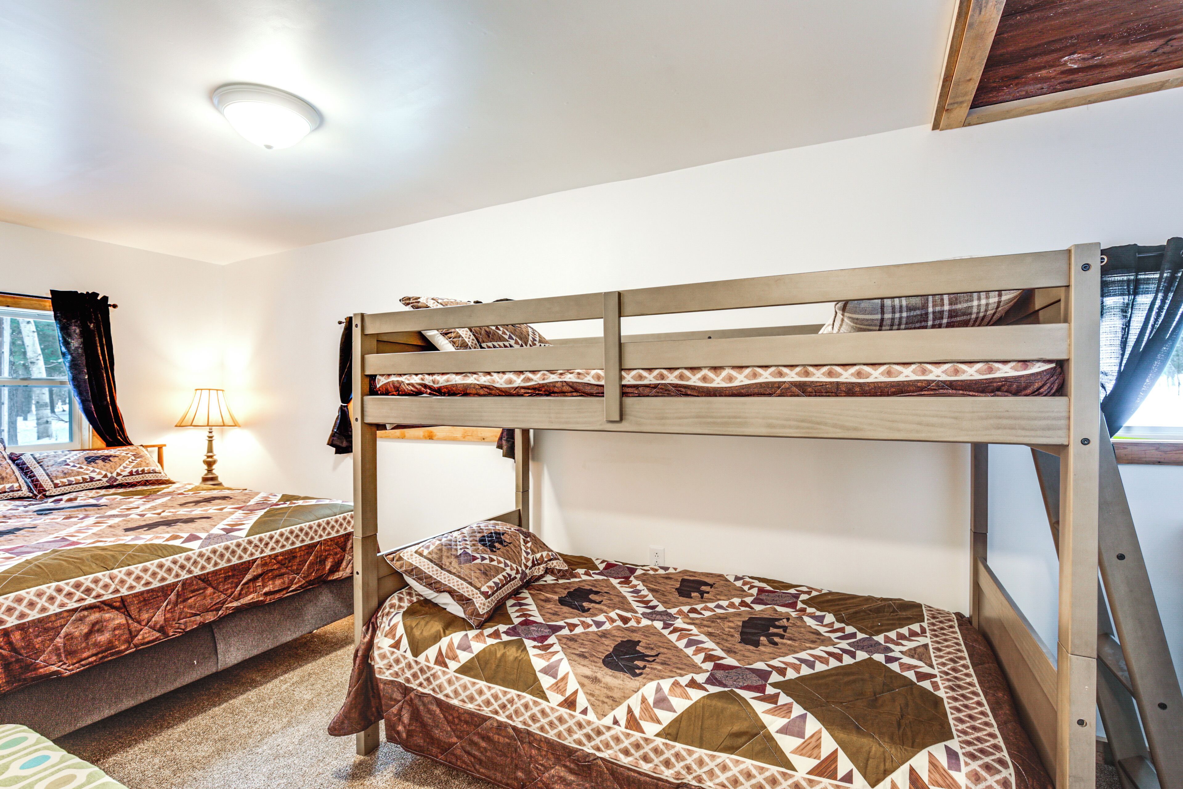 A bunk bed with a patterned quilt, a bedside lamp, and a window with curtains.