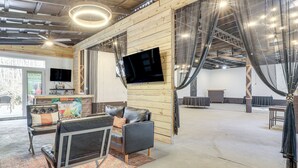 A spacious room with a large flat-screen TV mounted on a wooden wall, leather seating, and a patterned rug. - Georgia Farmhouse Studio w/ Hiking Trail (Lithonia)