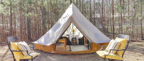 A tent with a dining table and two chairs in a forest setting.