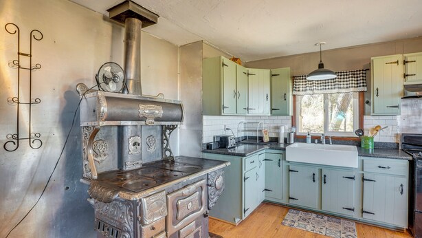 A kitchen with a vintage stove, light green cabinets, and a window with a checkered valance.