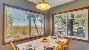 A dining area with a table set for four, large windows offering a view of a desert landscape, and a hanging light fixture above.