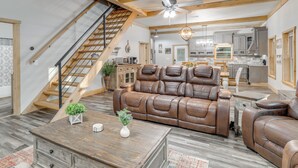 A spacious living area with a brown leather sofa, a wooden coffee table, and a staircase leading to an upper floor. - Greers Ferry Lake Access & Deck: Group Getaway! (Drasco)