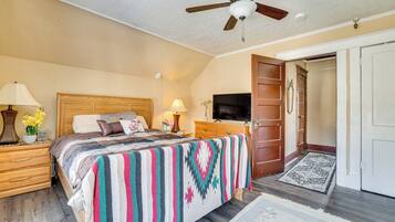 A bedroom with a bed, wooden headboard, bedside table with lamp, TV, and a door leading to another room.