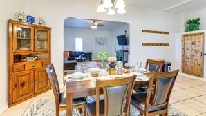Un coin repas avec une table en bois, dressée pour quatre personnes, entourée de chaises. Un buffet en bois, doté de portes en verre, se trouve à gauche.