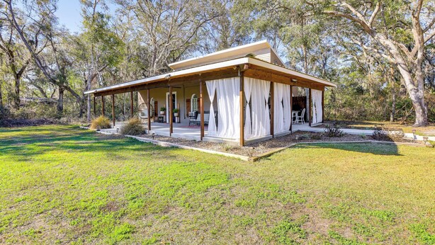 Une maison de plain-pied dotée d’un porche abrité, entourée d’une pelouse et d’arbres.