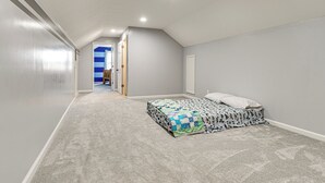 Une chambre avec un lit simple, une porte donnant sur une autre pièce et un sol recouvert de moquette.
