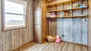 Une pièce d’angle avec des murs en bois, une fenêtre, une étagère avec des vêtements pliés et un panier contenant un jouet en peluche.