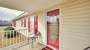 A covered porch with a red door, a white railing, and a welcome mat.