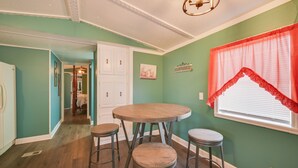 A dining area with a round table and four stools, a window with a red valance, and a hallway leading to another room.