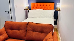 A room with a bed, orange upholstered sofa, and two bedside lamps. - Leicester Square 2nd Floor Studio (London)