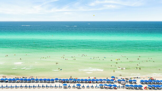 A beach with clear turquoise waters, a sandy shore, and numerous blue umbrellas. - Beachfront with unbeatable views, 3BR 2BA Condo at Sunrise Beach! (Panama City Beach)