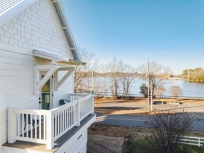 A white building with a balcony overlooking a body of water and a clear sky.