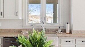 Una cucina con mobili bianchi, un piano di lavoro in granito, un lavello e una finestra che si affaccia su alberi.