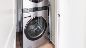 Una lavatrice e asciugatrice compatte in acciaio inox, all'interno di un piccolo locale lavanderia con pavimento in legno.