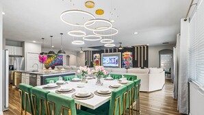 Eine moderne Küche mit Kochinsel, ein Essbereich mit dunkelgrünen Sesseln und ein Wohnzimmer mit großem Flachbildfernseher.