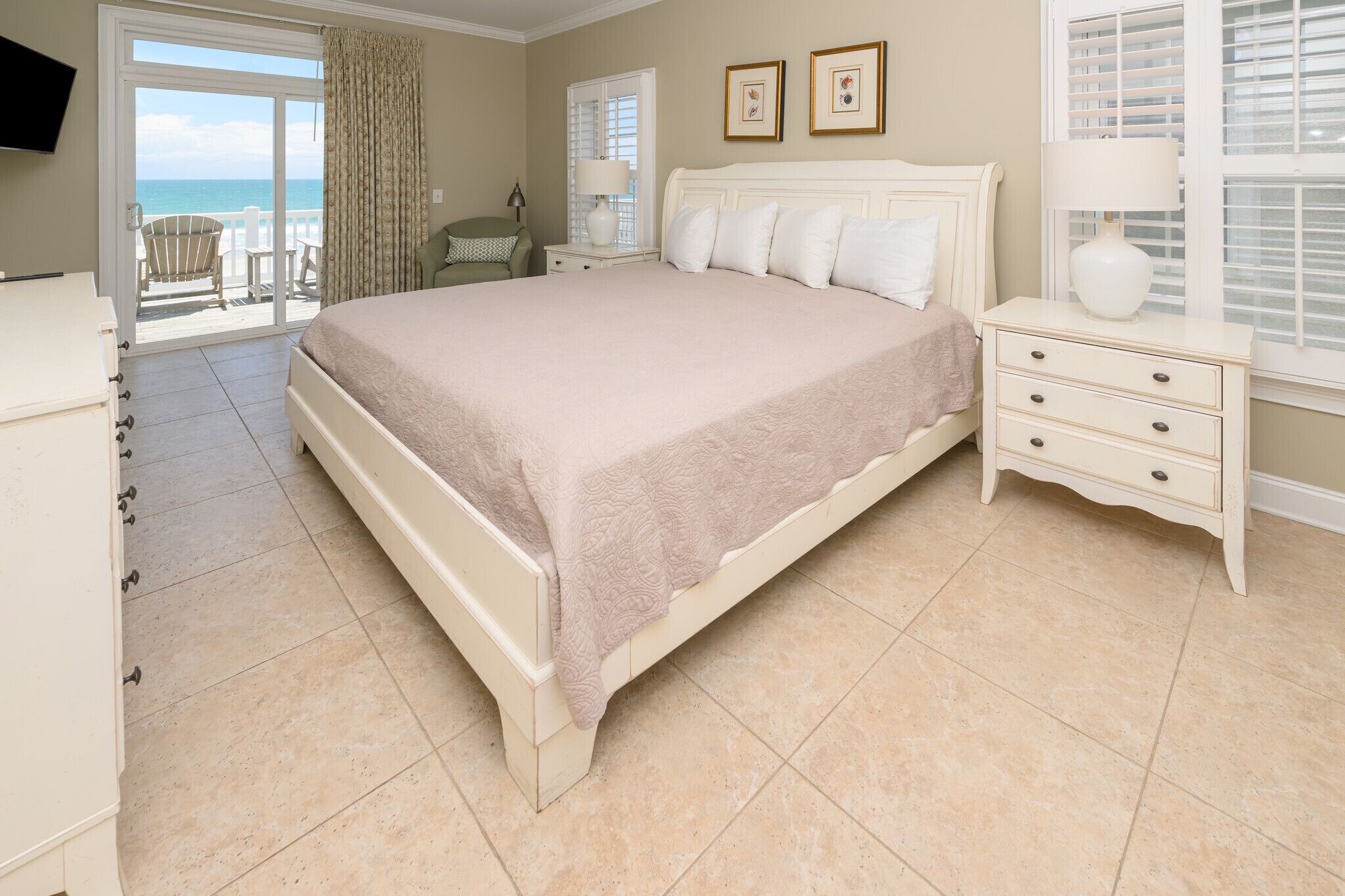 A bedroom with a large bed, a nightstand, a chair, a TV, and a view of the ocean.