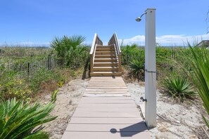 Una escalera de madera que conduce a una zona de playa con un poste de luz blanco y una estructura metálica.